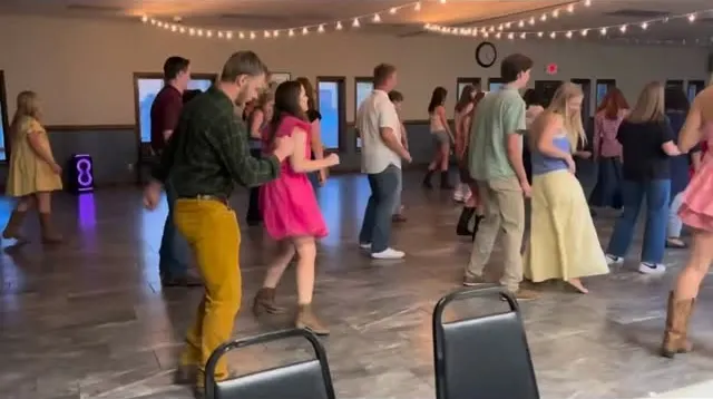 A full room of dancers line dancing under string lights at a Porch Swing social in Branson